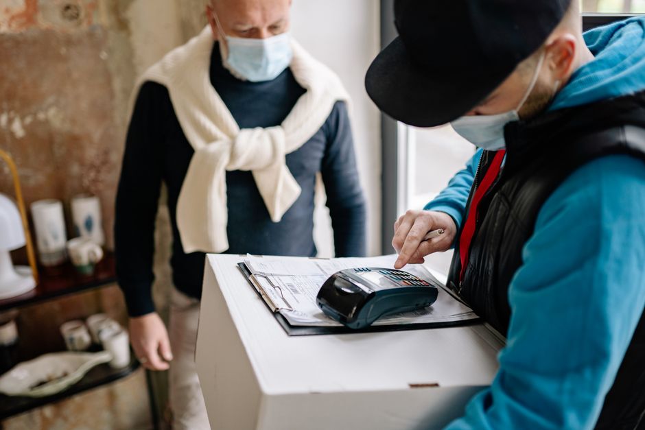 A delivery man and customer engage in a contactless transaction using a payment terminal.
